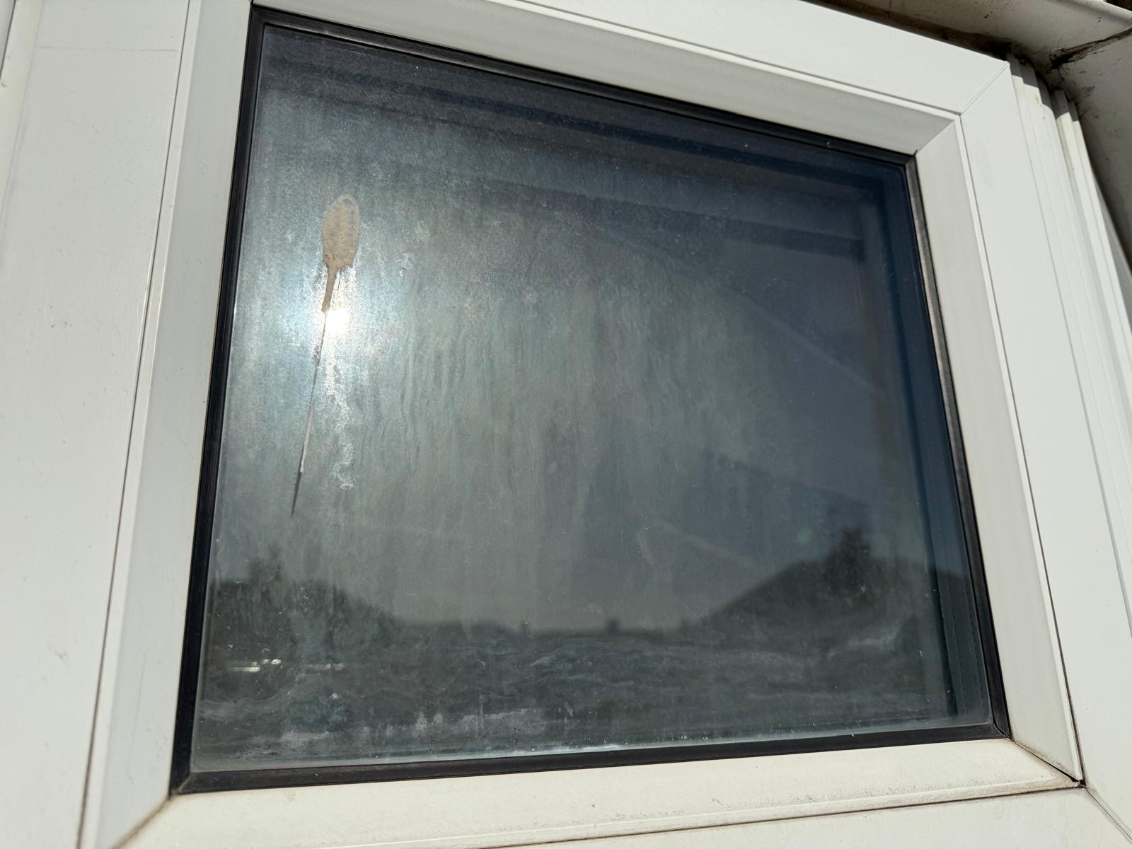 Before: a white uPVC window seen from outside, the sealed unit misted and heavily streaked where it has failed
